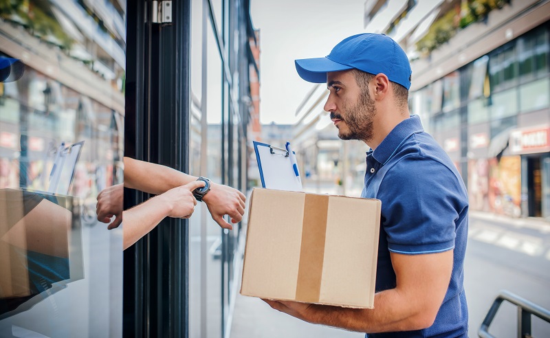 Entregador segura pacote enquanto cliente mostra o relógio, indicando atraso na entrega e a importância da gestão de frete reverso.